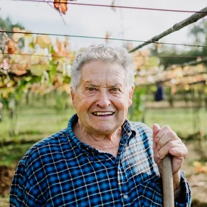 Antoine l'agriculteur se tenant debout dans son exploitation agricole bio avec le sourire et un outil à la main